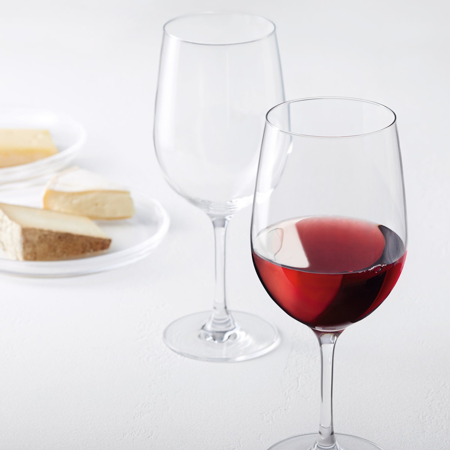 Rotweinglas CIAO+ mit Rotwein gefüllt, leeres Glas daneben, Käse und Brot im Hintergrund
