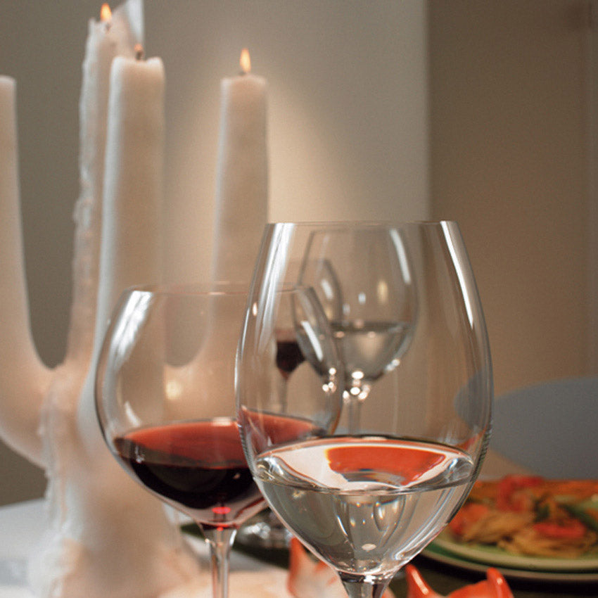 Weißweingläser CHEERS mit Rotwein auf gedecktem Tisch, Kerzen im Hintergrund