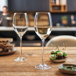 Zwei gefüllte Weißweingläser CHEERS auf Holztisch in Küchenumgebung
