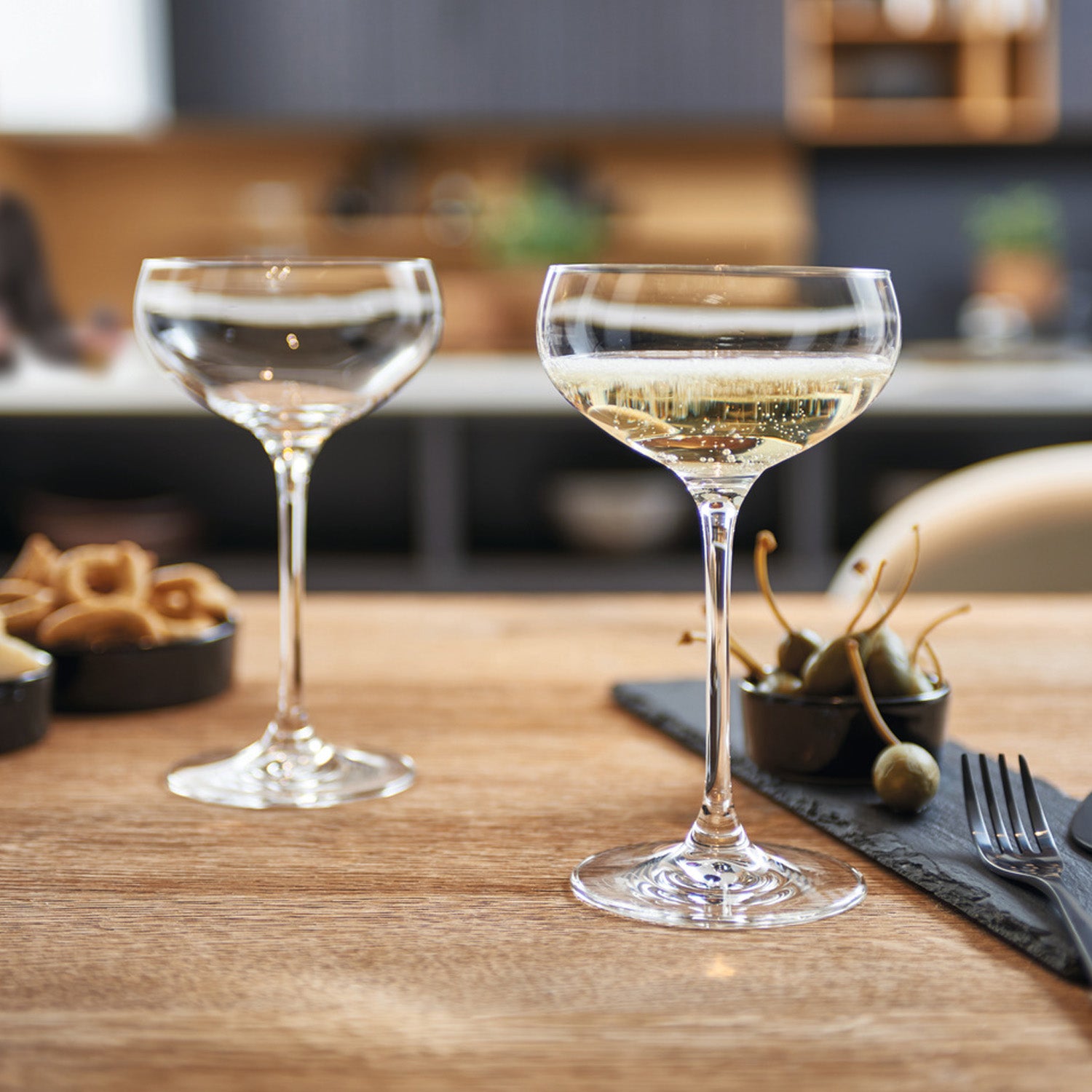 Zwei gefüllte Sektschalen CHEERS auf gedecktem Holztisch in Küche