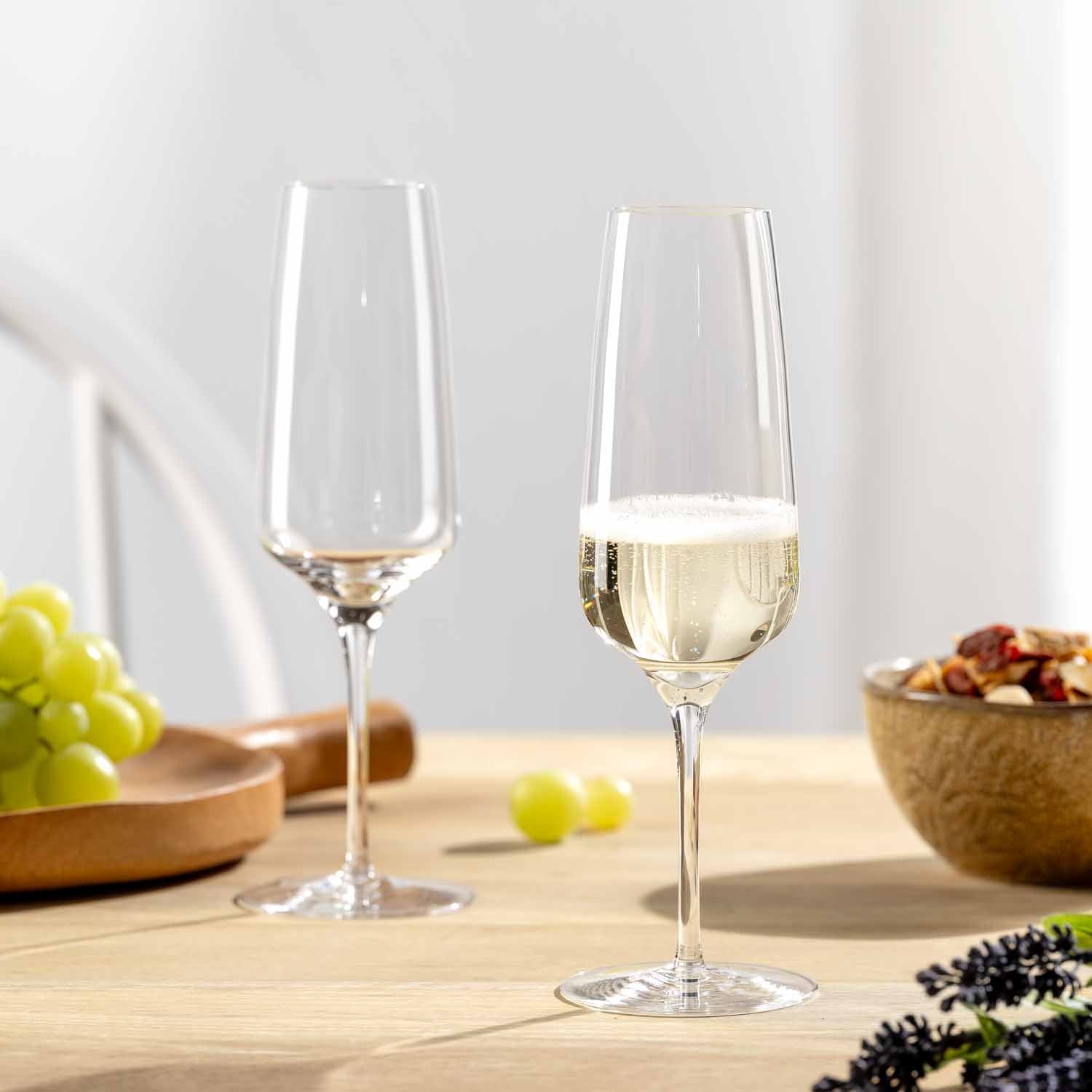 Sektglas CESTI mit Weißwein auf Holztisch, daneben Trauben und Nüsse