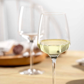 Rieslingglas 280 ml CESTI mit Weißwein gefüllt auf Holztisch, im Hintergrund weitere Gläser und Gebäck