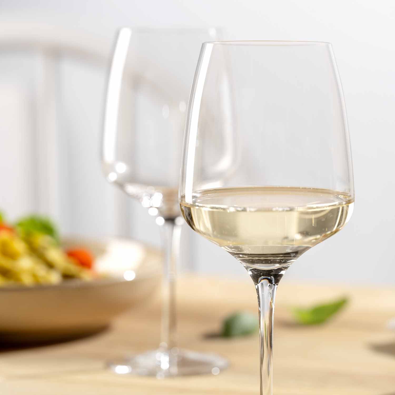 Weißweinglas CESTI mit Weißwein gefüllt, im Hintergrund weiteres Glas und Speisen auf Holztisch