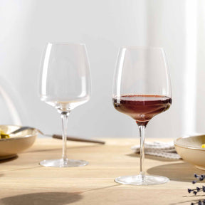 Zwei Rotweingläser CESTI auf gedecktem Tisch, eines leer, eines mit Rotwein gefüllt