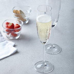 Zwei Sektgläser DAILY mit Champagner, daneben Gläser mit Erdbeeren und Keksen auf grauem Untergrund
