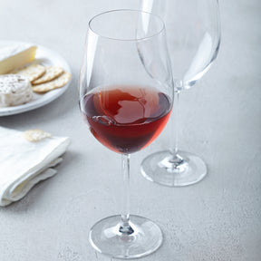 Bordeauxglas DAILY gefüllt mit Rotwein, daneben leeres Glas, gedeckter Tisch mit Käse und Crackern