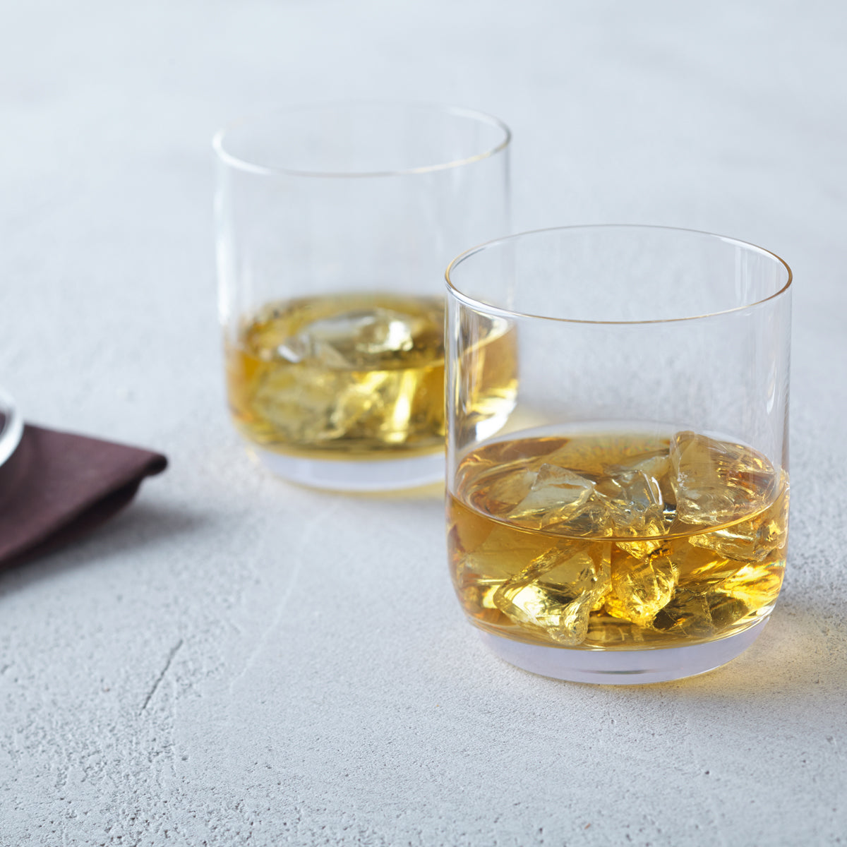 Zwei Trinkgläser DAILY mit Whiskey und Eiswürfeln auf grauem Untergrund