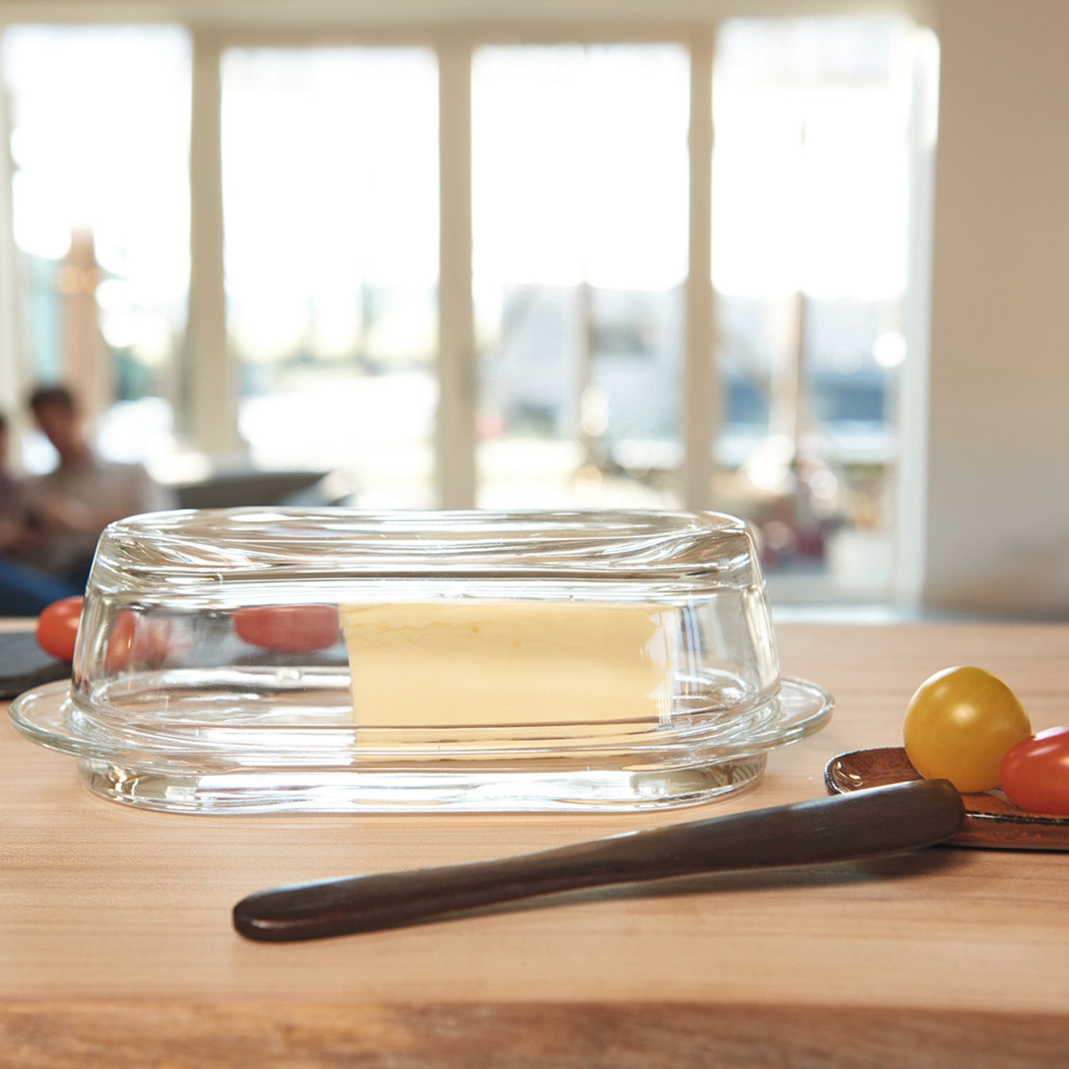 Butterdose CIAO aus Glas mit Butter auf Holztisch, Buttermesser daneben, helles Tageslicht von Fensterfront