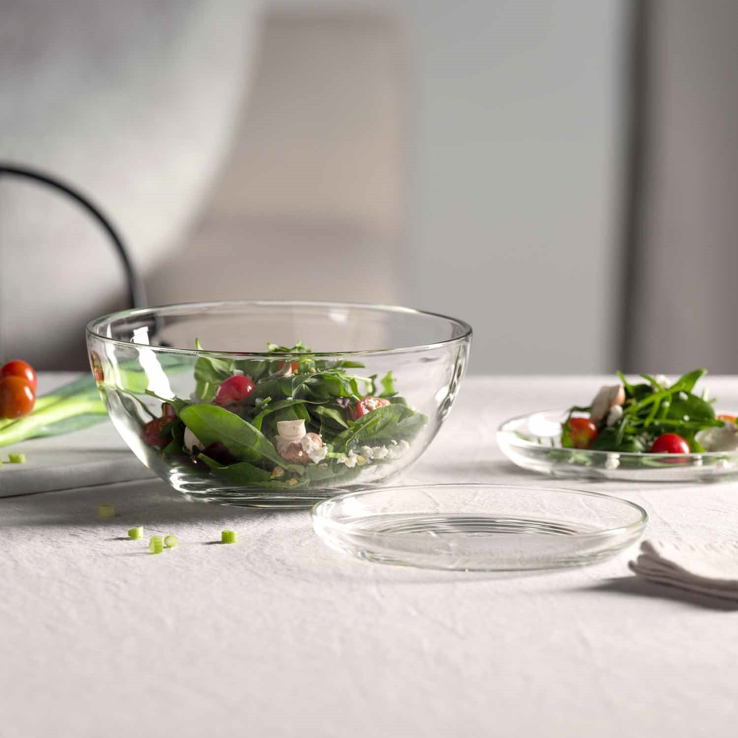 Glasteller und Glasschalen mit Salat auf gedecktem Tisch