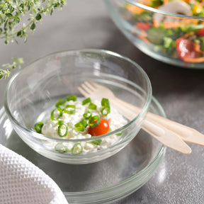 Glasschale mit Salatzutaten und Besteck auf grauem Untergrund