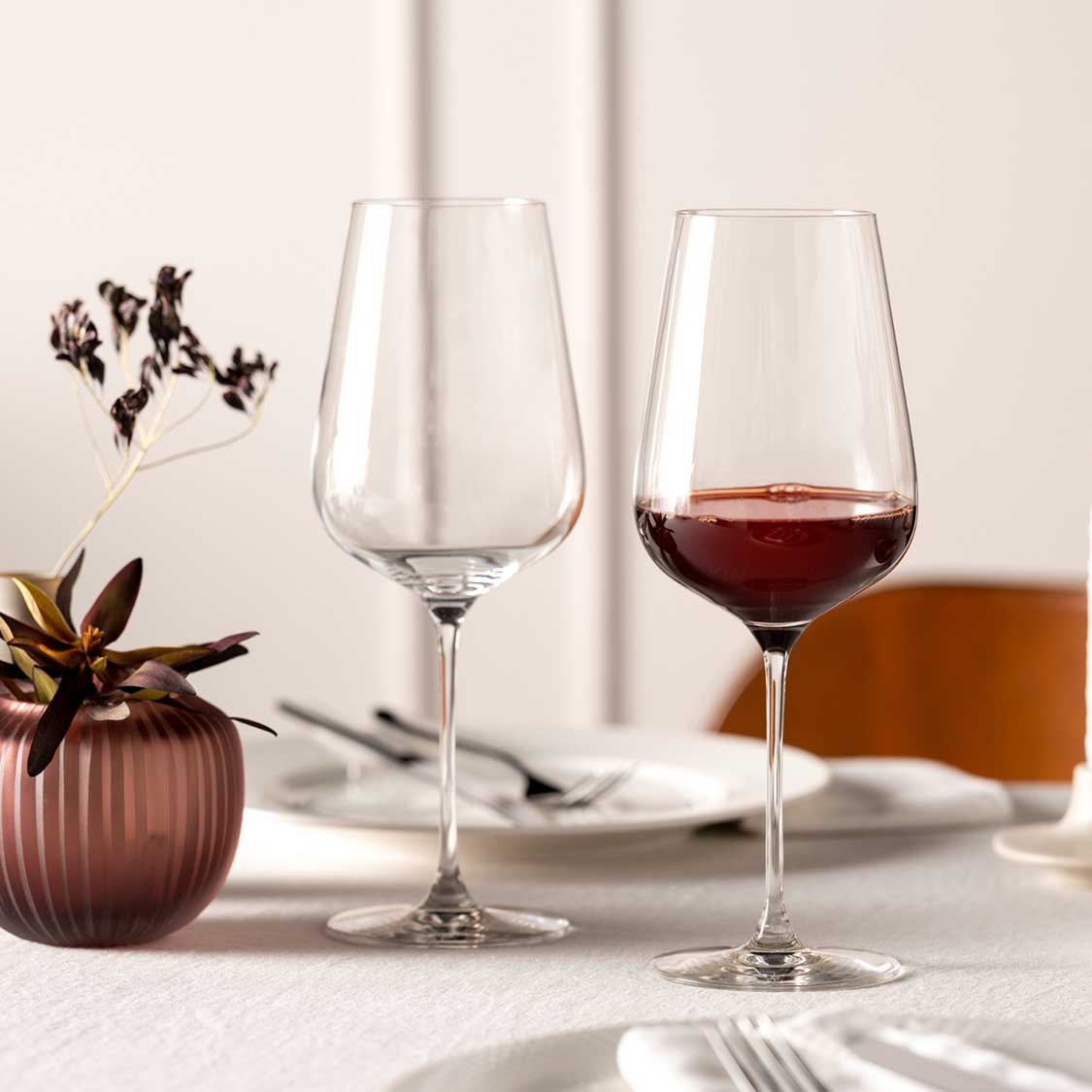 Rotweinglas BRUNELLI auf gedecktem Tisch, eines gefüllt mit Rotwein, neben Blumenvase und Gedeck