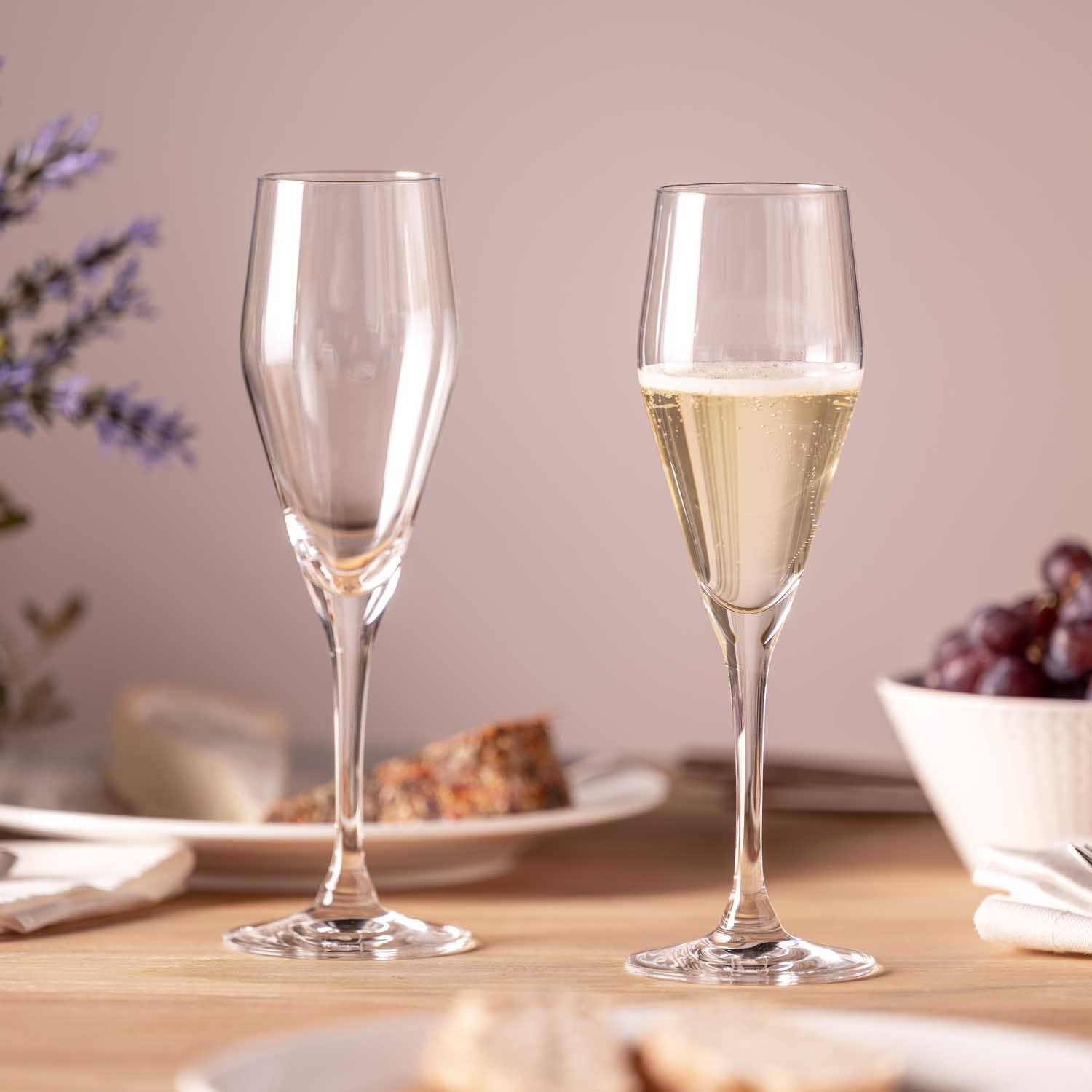 Zwei Sektgläser TWENTY 4, eines leer und eines mit Sekt gefüllt, auf gedecktem Tisch mit Blumen