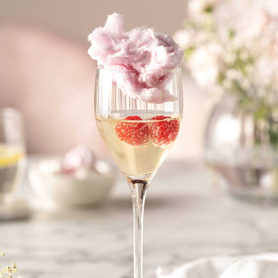 Likörglas POESIA mit Champagner, Himbeeren und rosa Zuckerwatte, dekorativ gedeckter Tisch
