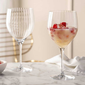 Zwei Cocktailgläser POESIA auf Marmortisch, eines leer, eines mit Getränk und Himbeeren gefüllt