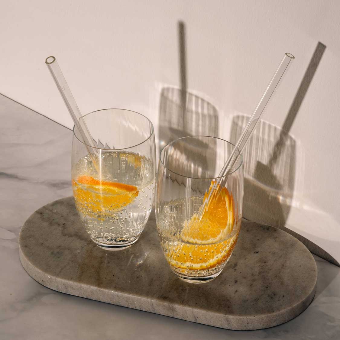 Trinkgläser POESIA mit Orangenscheiben, Strohhalmen auf Betonplatte
