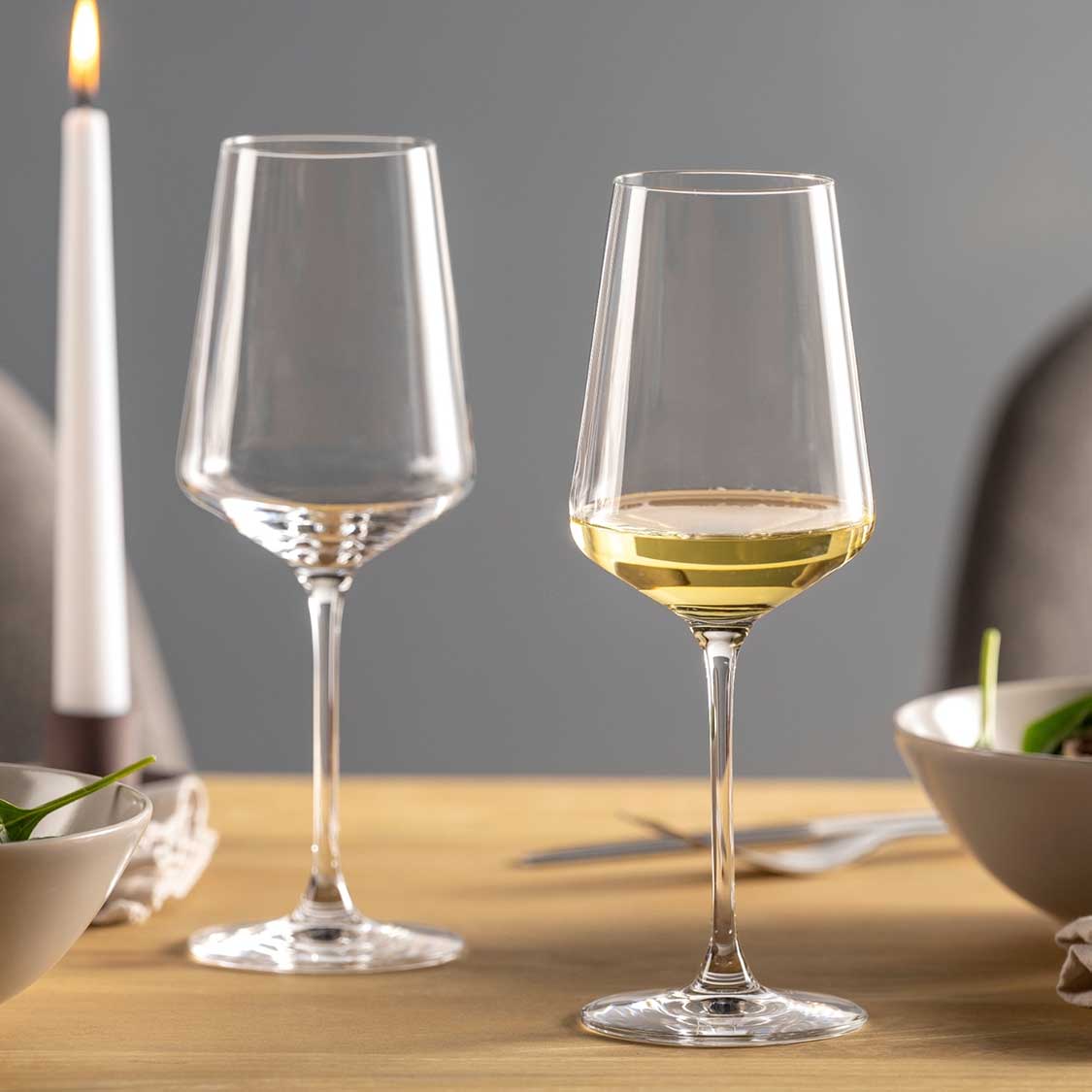 Zwei Rieslinggläser PUCCINI auf Holztisch, eines leer, eines mit Weißwein gefüllt, daneben brennende Kerze