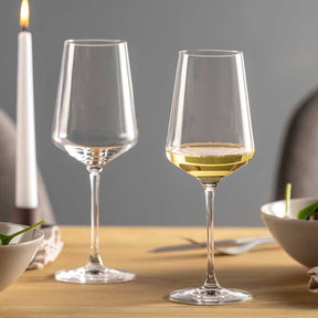 Zwei Rieslinggläser PUCCINI auf Holztisch, eines leer, eines mit Weißwein gefüllt, daneben brennende Kerze