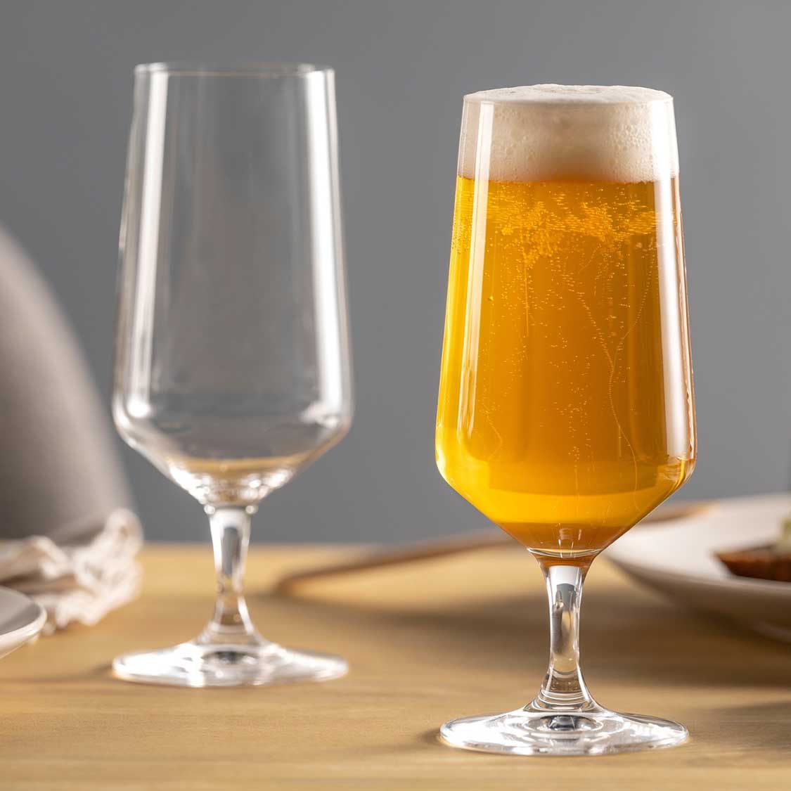 Zwei Biergläser PUCCINI auf Holztisch, eines leer, eines mit Bier gefüllt
