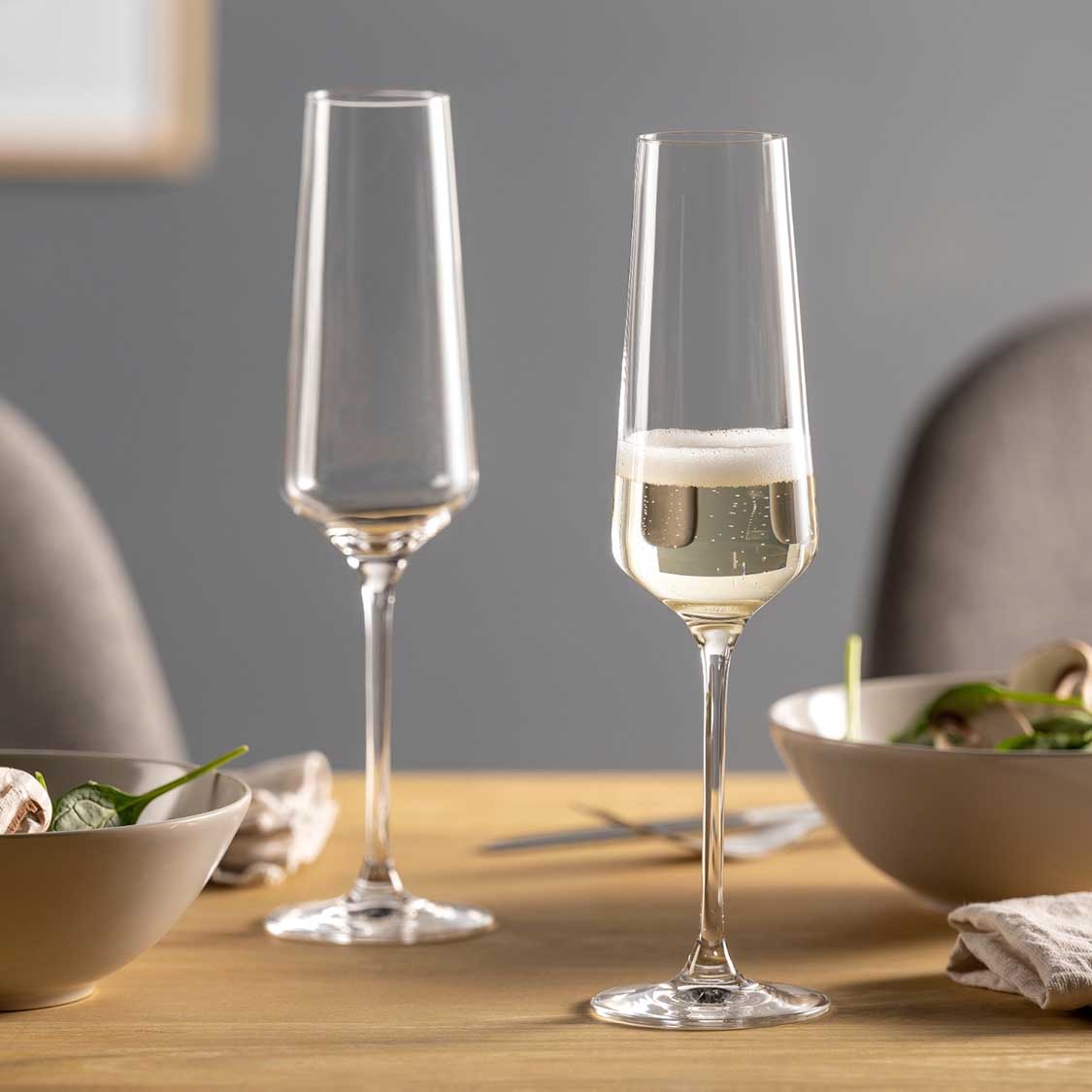 Zwei Sektgläser PUCCINI auf gedecktem Tisch, eines leer, eines mit Sekt gefüllt