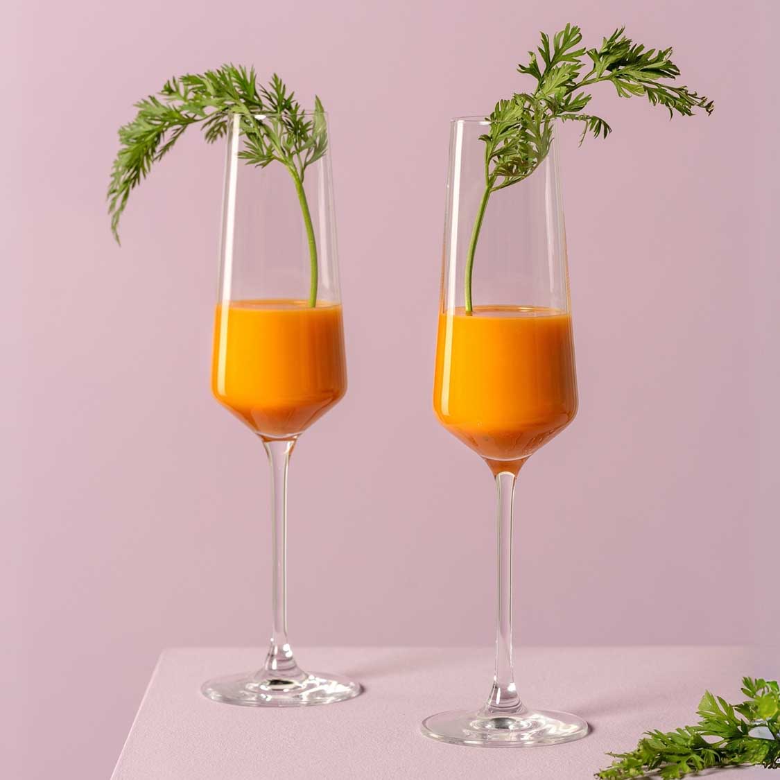 Zwei Sektgläser PUCCINI mit orangefarbenem Getränk und Kräuterdekoration auf rosa Hintergrund