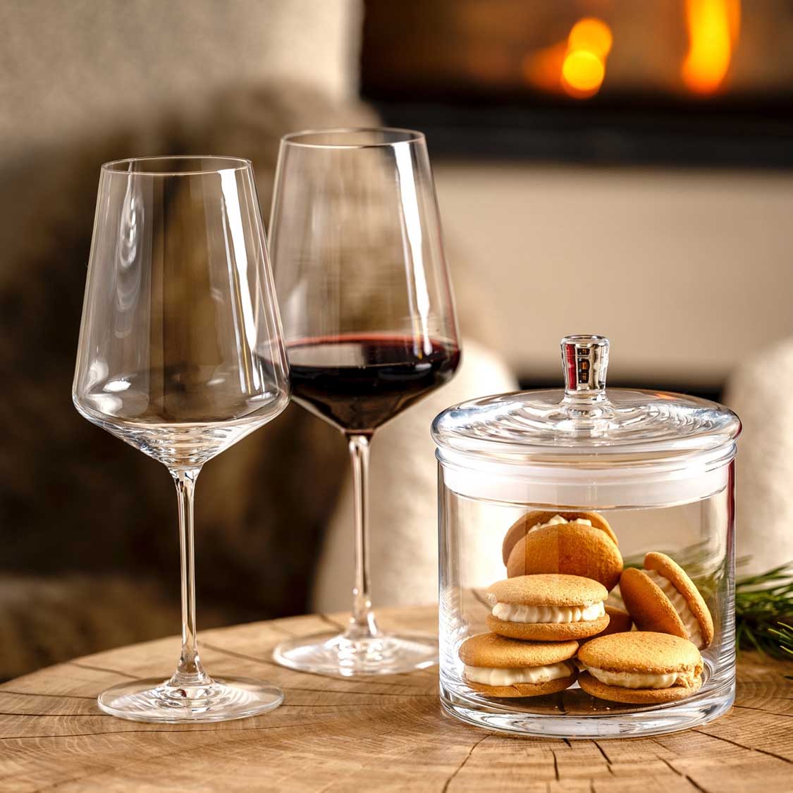 Rotweinglas PUCCINI mit Rotwein auf Holztisch neben Keksdose und Kerzen