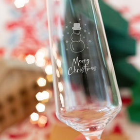 Sektglas PUCCINI mit Schneemann-Gravur und "Merry Christmas"-Schriftzug, festliche Dekoration im Hintergrund
