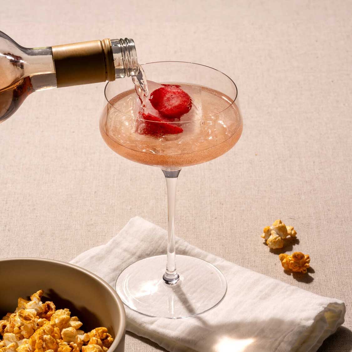Champagnerschale PUCCINI wird gefüllt, mit Erdbeere und Eiswürfeln, neben Popcorn und Serviette
