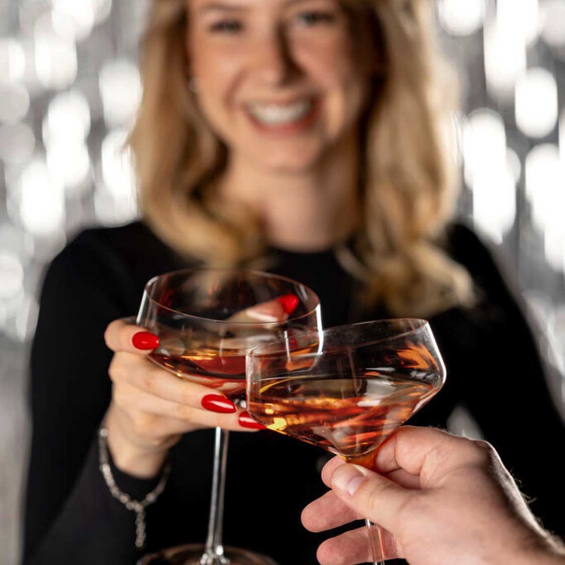 Zwei Champagnerschalen PUCCINI werden von zwei Personen zum Anstoßen gehoben, gefüllt mit bernsteinfarbenem Getränk