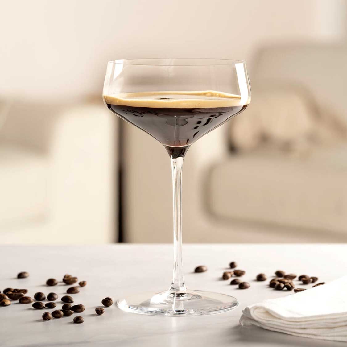 Champagnerschale PUCCINI mit Kaffeelikör gefüllt, daneben Kaffeebohnen auf weißer Oberfläche