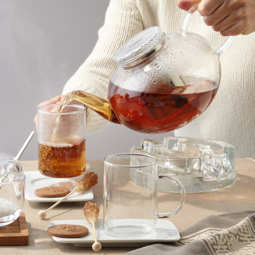Teekanne MOON wird über Tasse mit Tee eingegossen, gedeckter Tisch mit Gebäck