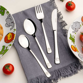 Kinderbesteck BAMBINI 4-teilig silber auf grauem Tuch, arrangiert mit Tellern und Tomaten