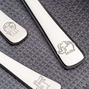 Kinderbesteck BAMBINI 4-teilig mit gravierten Tiermotiven Löwe, Elefant, Krokodil auf grauem Textiluntergrund