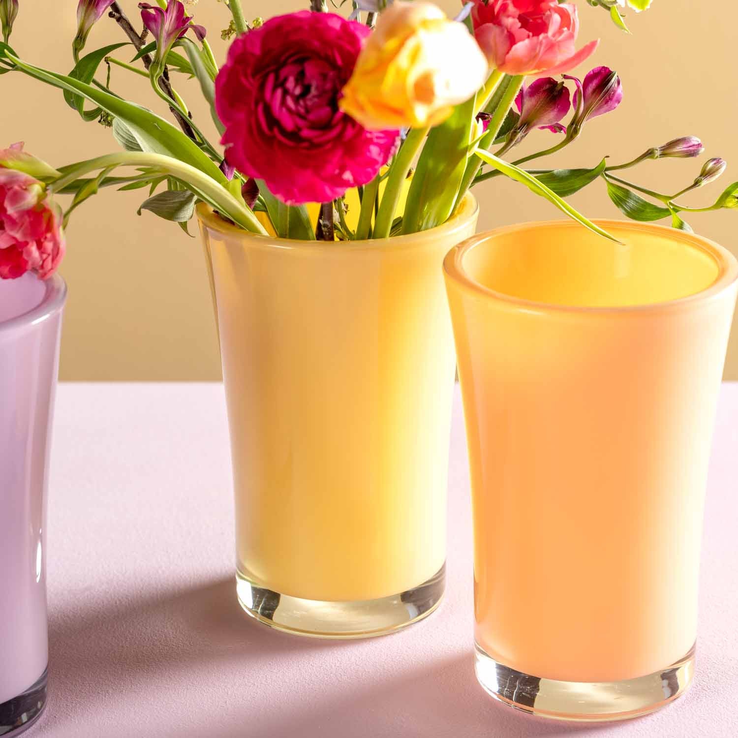 Glasvasen mit Schnittblumen auf Tisch mit Sonnenlicht