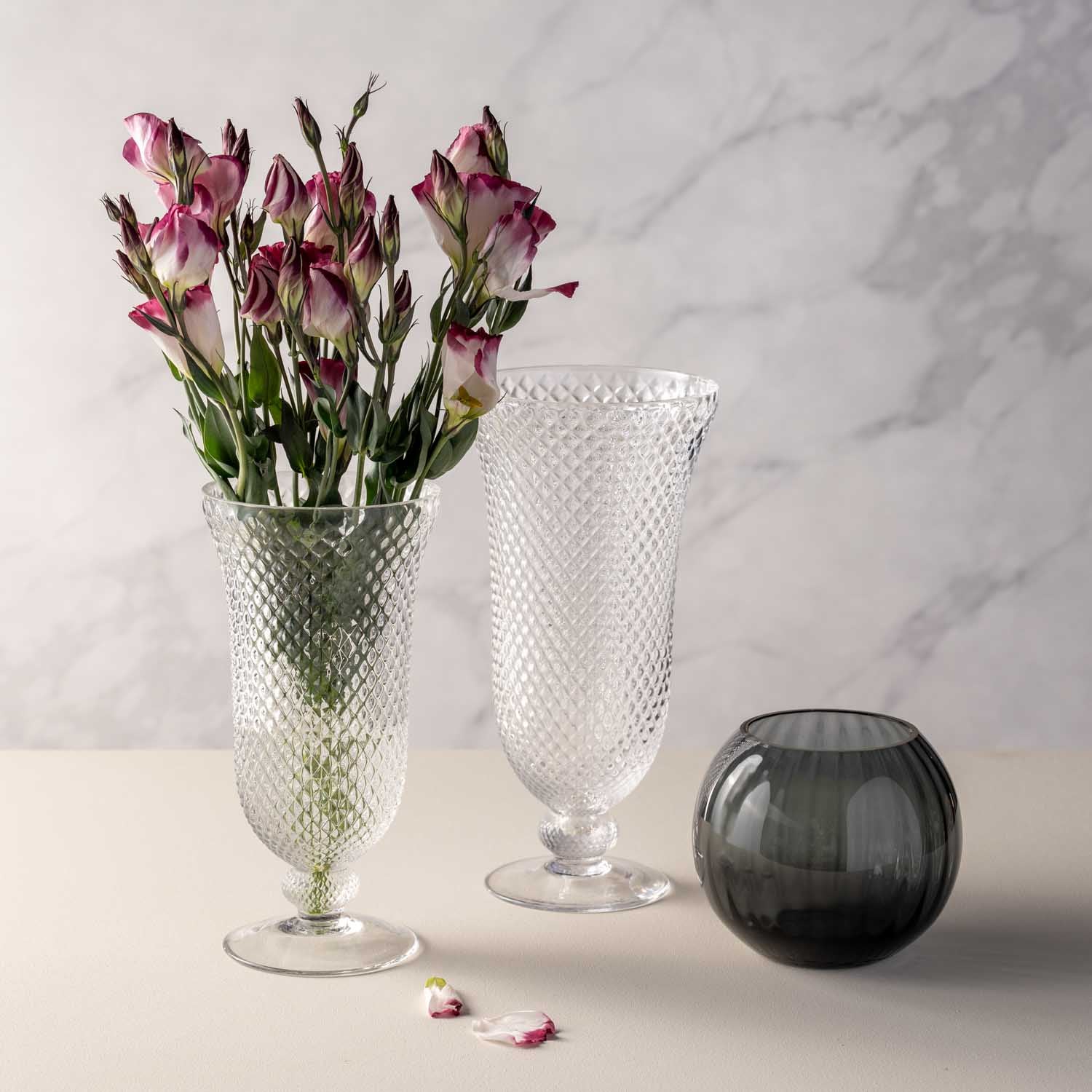 Vase auf Fuß POESIA mit rosa Nelken, daneben leere Vase und schwarze Kugelvase auf Marmortisch