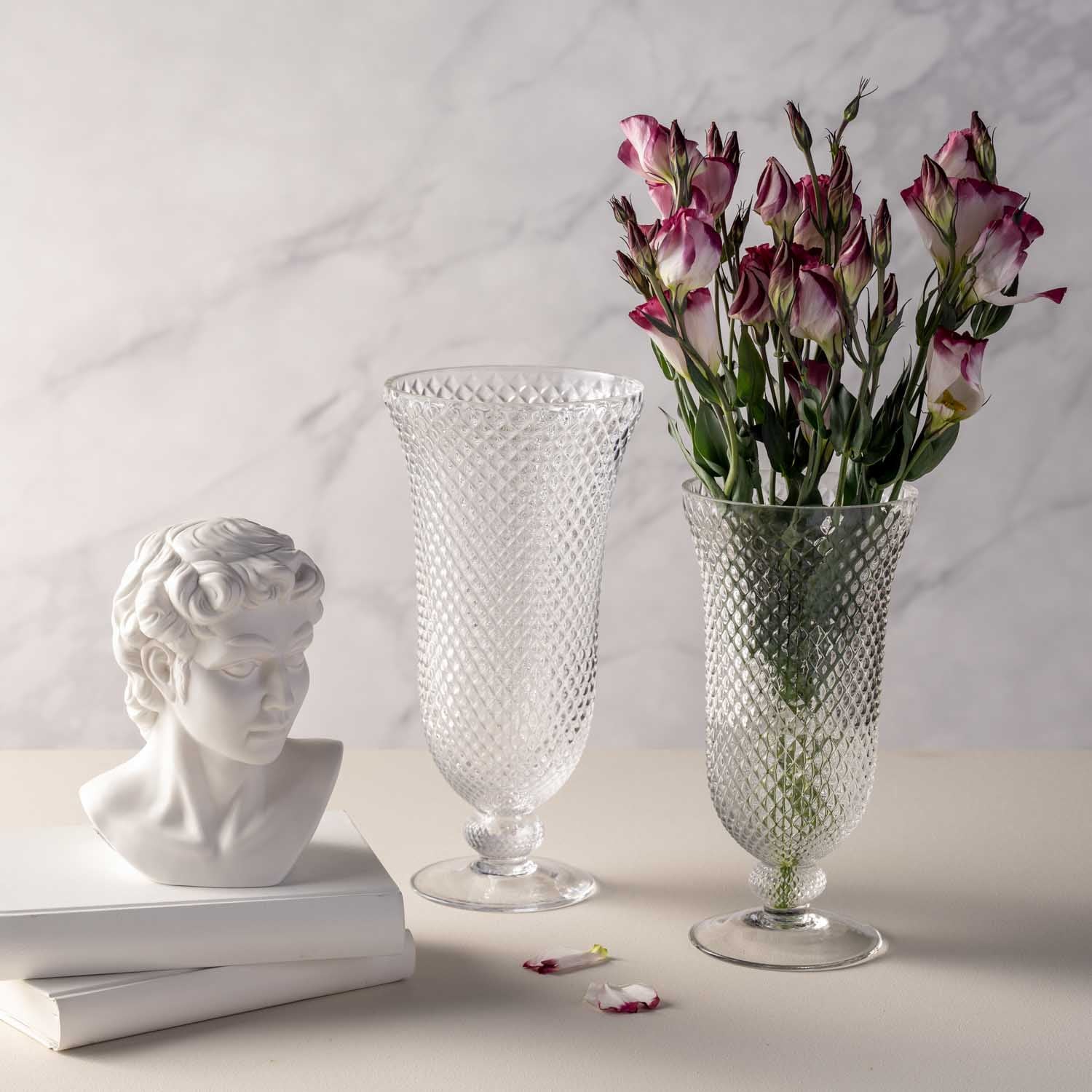 Vase auf Fuß POESIA mit rosa Blüten, neben Büsten und Dekoobjekten auf Marmor