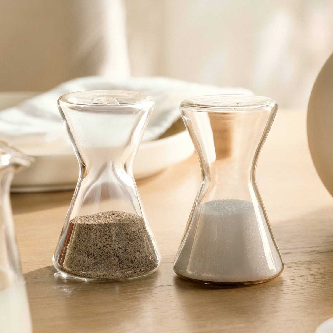 Zwei Salz & Pfefferstreuer GIORNO aus Glas auf Holztisch, Tischgedeck im Hintergrund