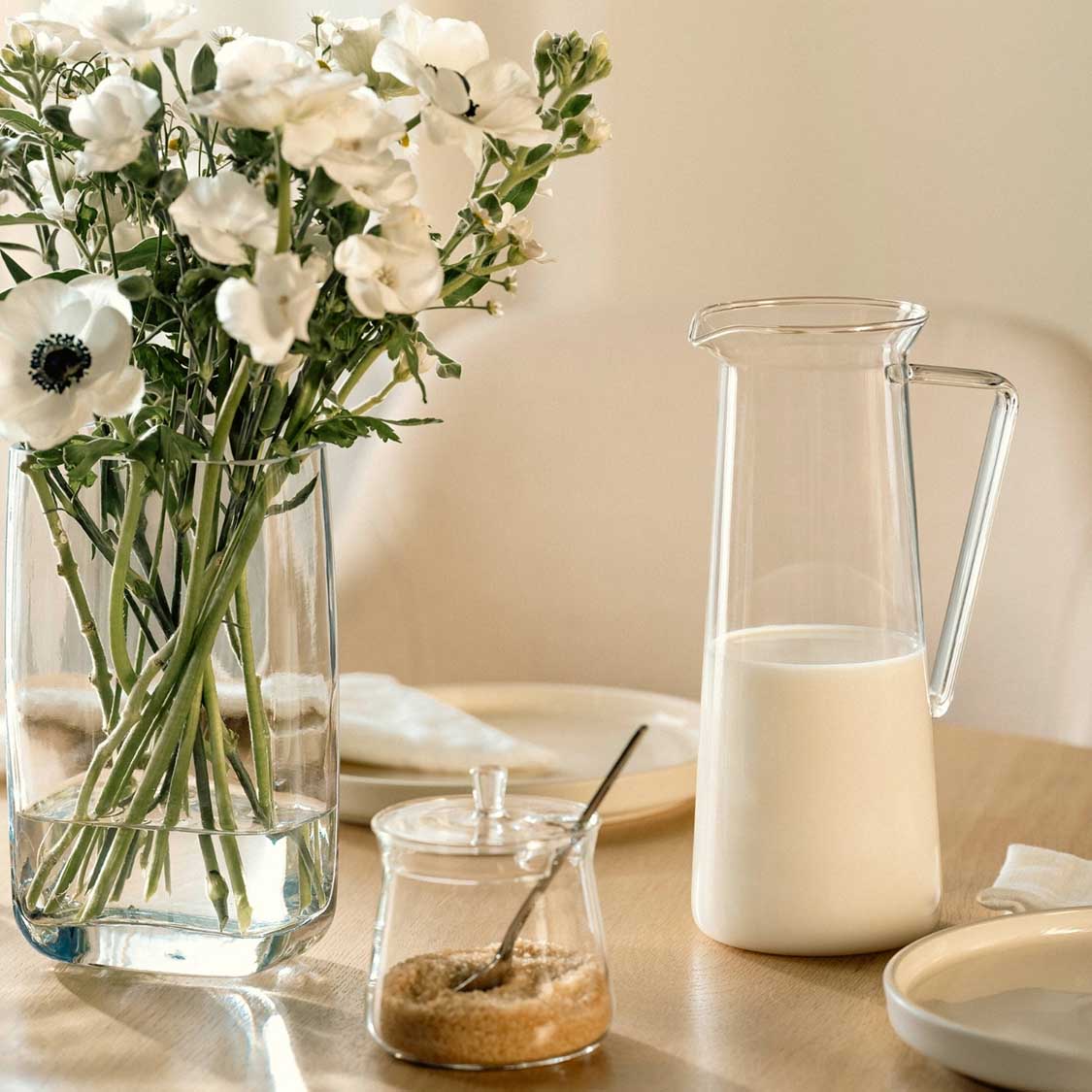 Krug GIORNO mit Milch auf gedecktem Tisch neben Blumenvase