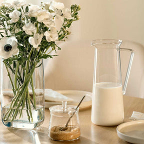 Krug GIORNO mit Milch auf gedecktem Tisch neben Blumenvase
