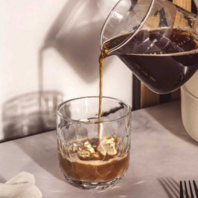 Kännchen GIORNO gießt Kaffee in Glas mit Eiswürfeln, gedeckter Tisch