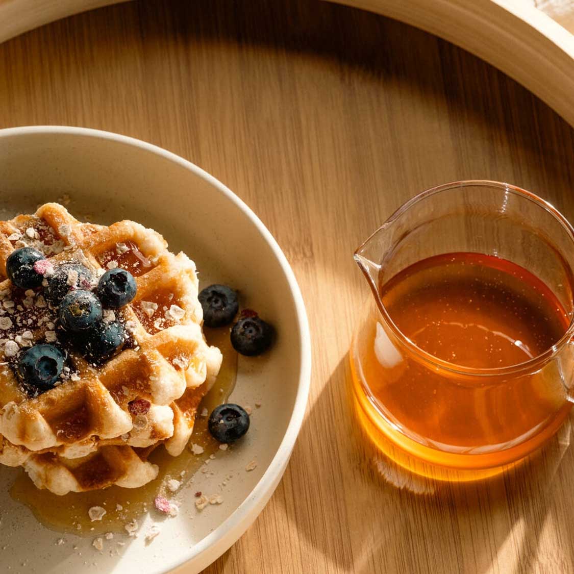 Kännchen GIORNO mit Honig neben Waffeln und Blaubeeren auf Holztisch