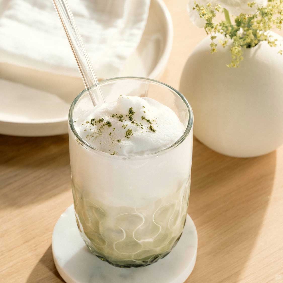 Matcha Latte Glas GOCCE mit Glastrinkhalm gefüllt auf Holztisch mit Deko