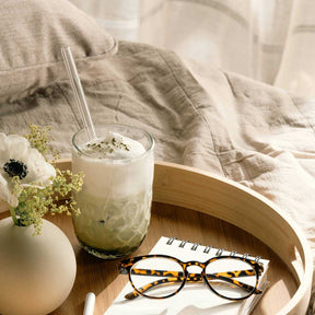 Matcha Latte Glas GOCCE mit Glastrinkhalm auf Holztablett, Blumen und Brille