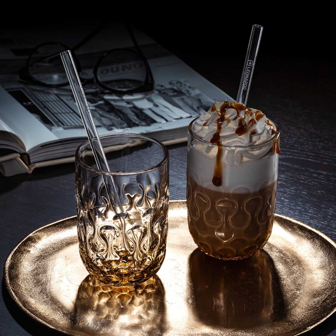 Caramel Macchiato Gläser GOCCE mit Glastrinkhalmen auf Goldtablett, Buch und Lupe im Hintergrund