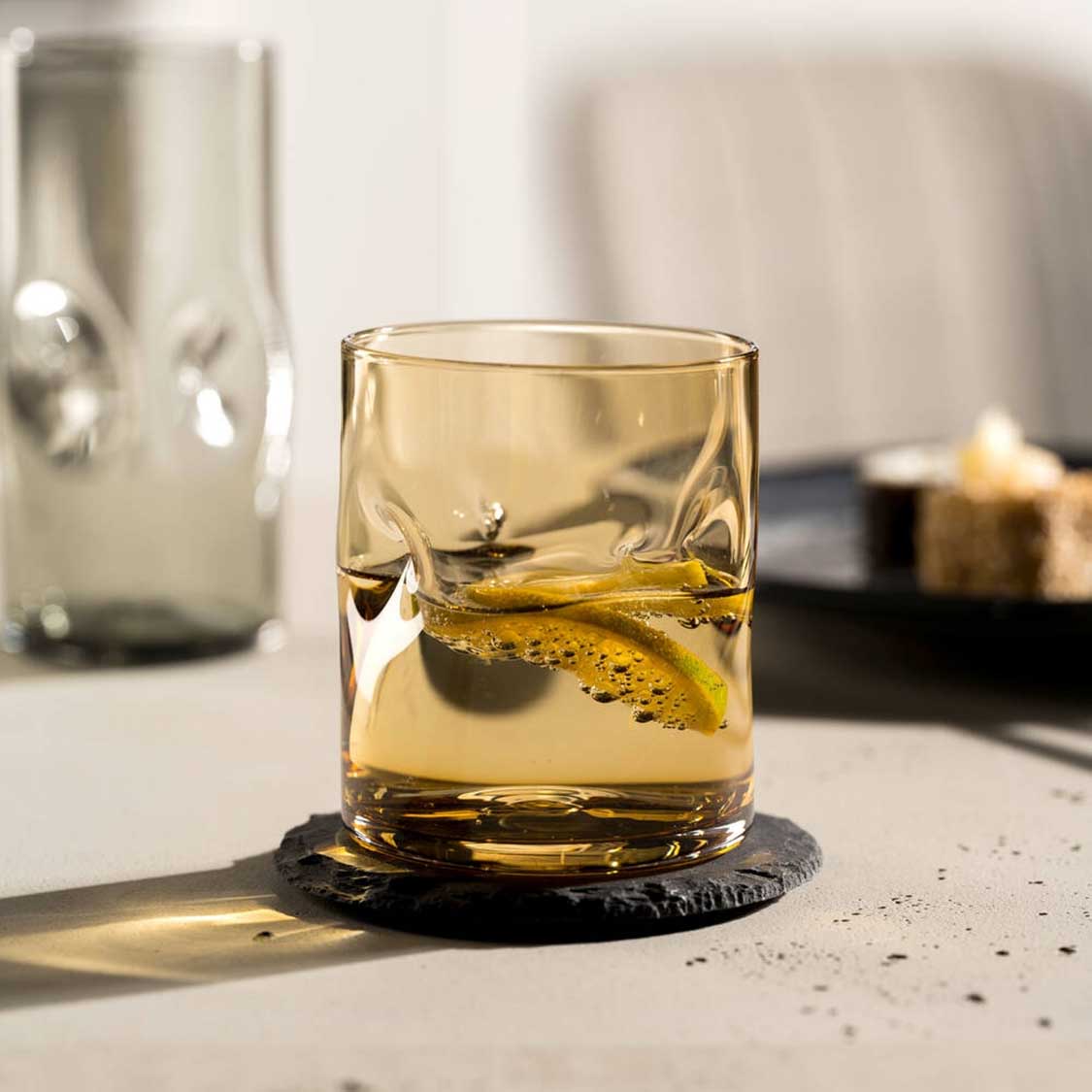 Trinkglas VESUVIO mit Whiskey und Eiswürfel auf schwarzem Untersetzer, Schreibtisch mit Deko