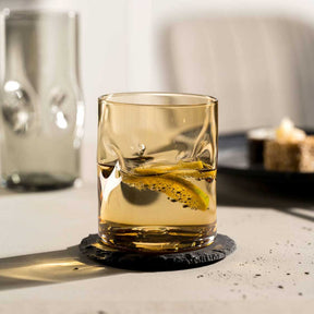 Trinkglas VESUVIO mit Whiskey und Eiswürfel auf schwarzem Untersetzer, Schreibtisch mit Deko