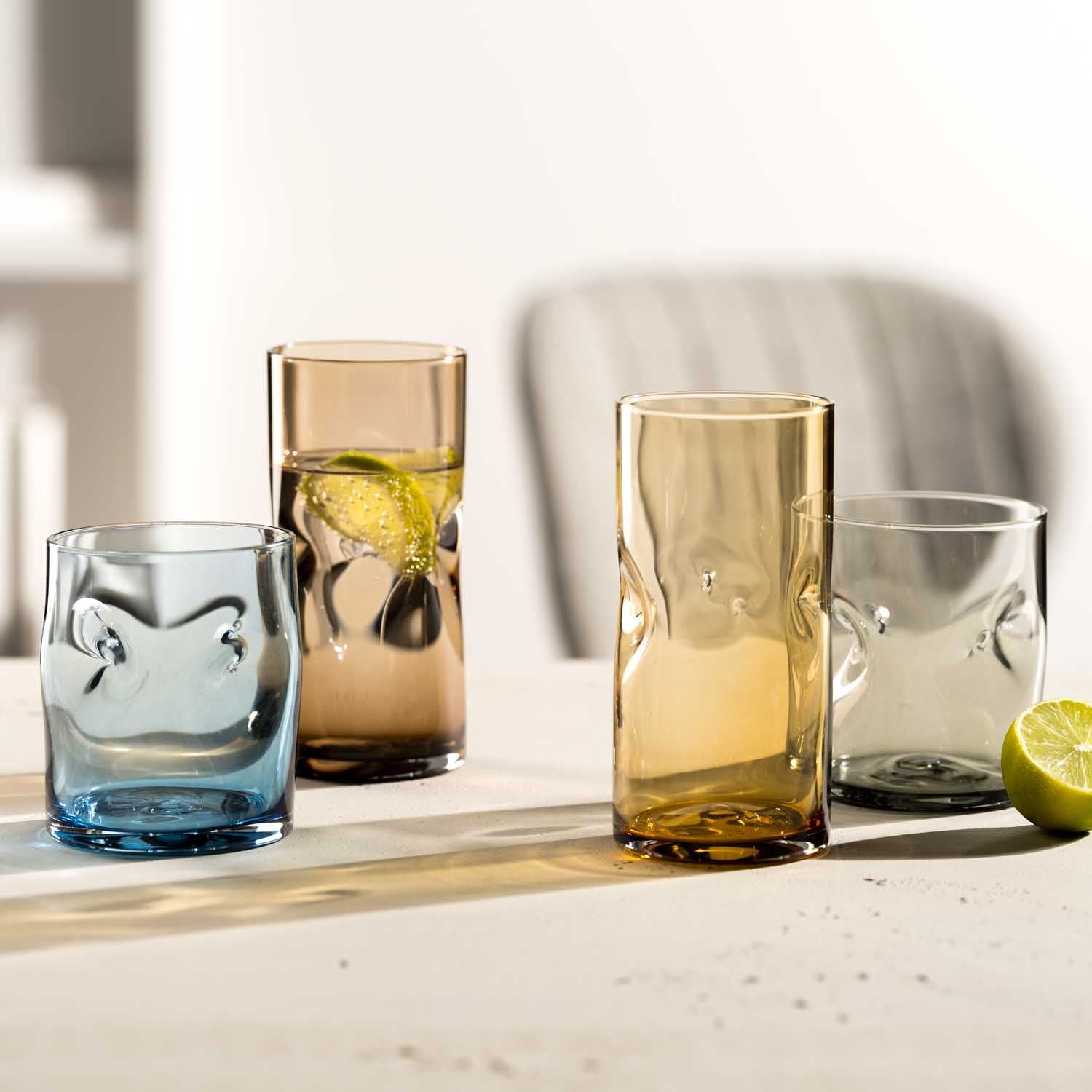 Trinkgläser VESUVIO in Amber und Blau mit Wasser, Limette und Getränken auf heller Oberfläche
