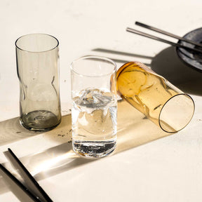 Trinkgläser mit Wasser und Flasche, Besteck und Schatten auf hellem Untergrund