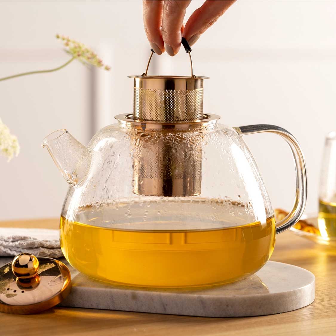 Teekanne TÈ PER TE mit kochendem Wasser, Sieb wird herausgenommen, Tisch mit Deko