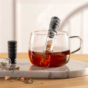 Glastasse mit Tee auf Marmortablett, Teesieb und Teedose daneben