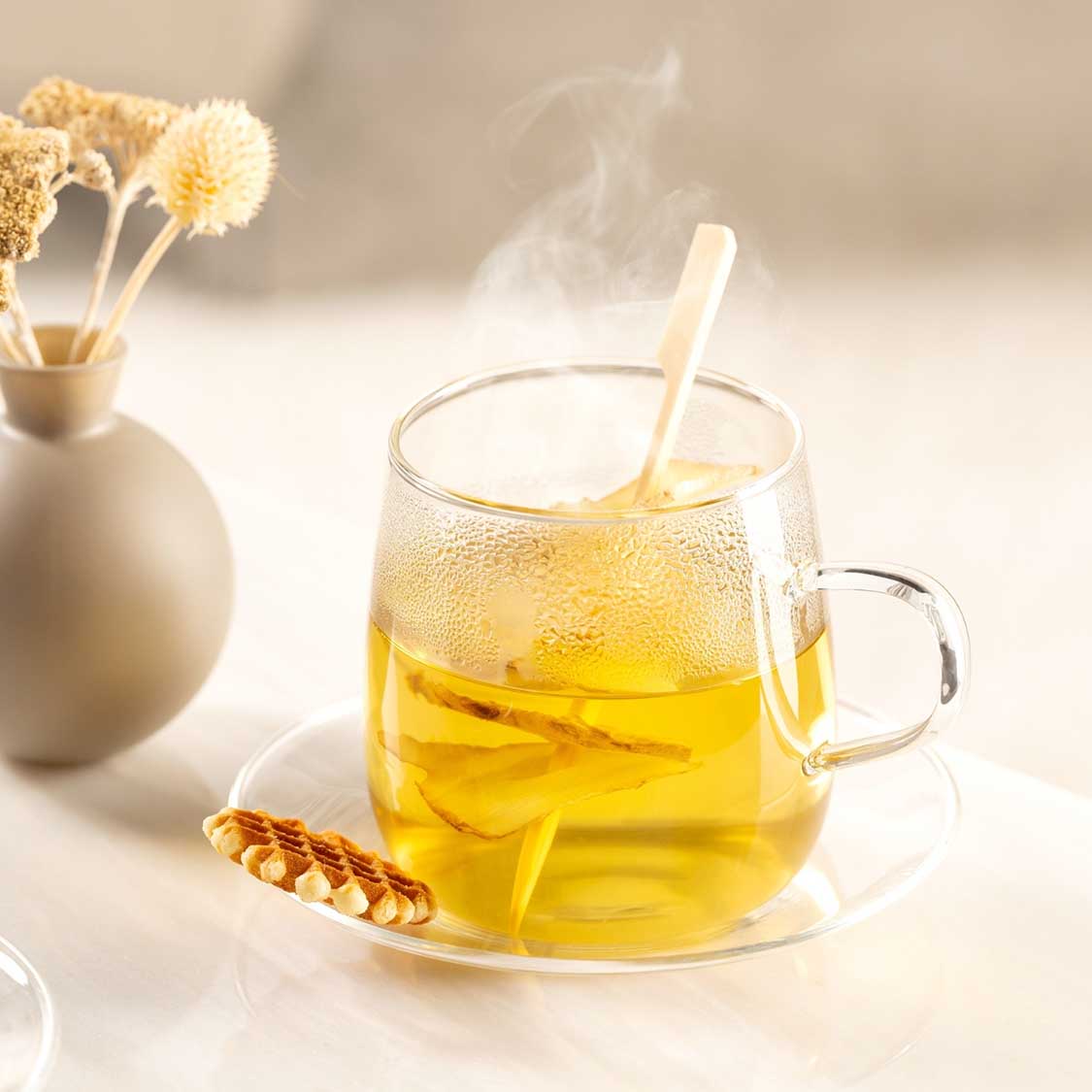 Teetasse mit dampfendem Tee, Löffel, Trockenblumen und Honig in warmer Tischszene